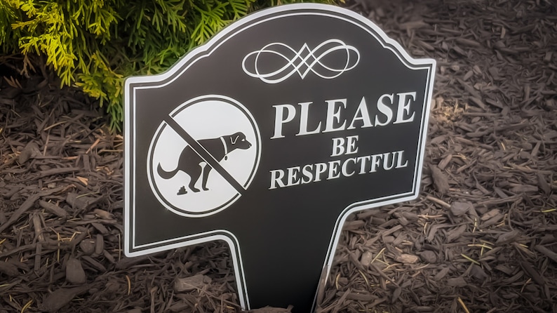 A small yard sign with the message Please Be Respectful and a no dog pooping symbol.  It has a stake that is used to plant the sign in the ground.  A sleek black finish with bright white text makes this sign a very attractive addition to your yard.