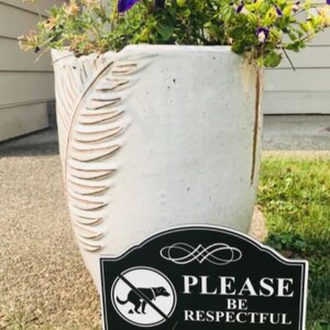 A small yard sign with the message Please Be Respectful and a no dog pooping symbol.  It has a stake that is used to plant the sign in the ground.  A sleek black finish with bright white text makes this sign a very attractive addition to your yard.