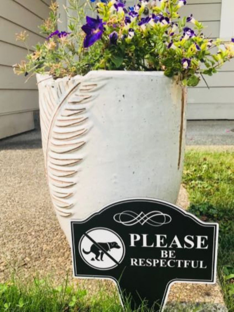 A small yard sign with the message Please Be Respectful and a no dog pooping symbol.  It has a stake that is used to plant the sign in the ground.  A sleek black finish with bright white text makes this sign a very attractive addition to your yard.