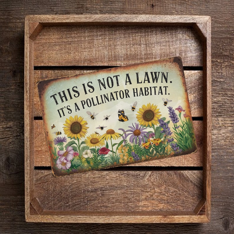May include: A rustic wooden sign with the text "This is not a lawn. It's a pollinator habitat."  The sign features a colorful illustration of a garden with sunflowers, butterflies, and bees.