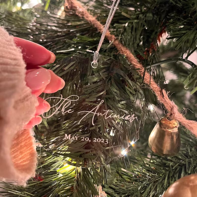 May include: A clear glass Christmas ornament with the text "The Antunes" and "MAY 20, 2023" etched in white.