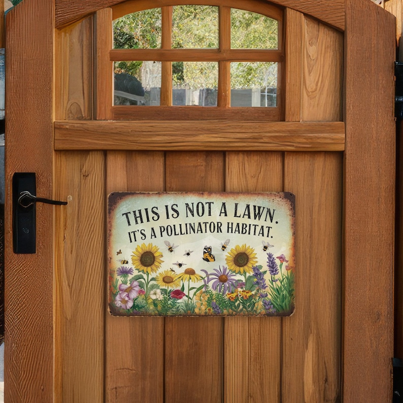 May include: A metal sign with a white background and a green border. The sign reads "This is not a lawn. It's a pollinator habitat." and features a colorful illustration of sunflowers, bees, and butterflies.
