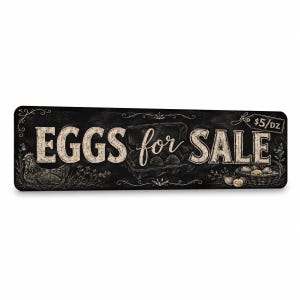 May include: A rectangular black sign with white chalk-style illustrations and text. The sign features a hen, a carton of eggs, and a basket of eggs. The text reads "EGGS for SALE" in large lettering, with a small tag in the corner stating "$5/DZ".