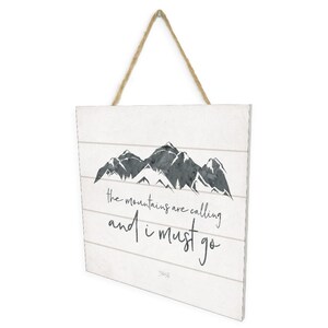 May include: A white wooden sign with a black and gray watercolor mountain range illustration. The sign has the text "the mountains are calling and i must go" written in black cursive font.