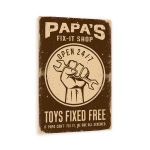 May include: A vintage-style metal sign with a brown background and white text. The sign reads "Papa's Fix-It Shop" and features a hand holding a wrench inside a circle with the text "Open 24/7". The sign also says "Toys Fixed Free" and "If Papa can't fix it, we are all screwed."