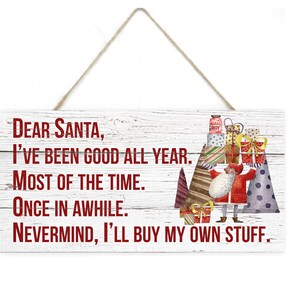 May include: White wooden sign with red text that reads "Dear Santa, I've been good all year. Most of the time. Once in awhile. Nevermind, I'll buy my own stuff."  A cartoon Santa Claus is holding a stack of presents with a candy cane on top.