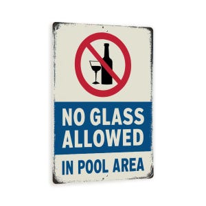 May include: A blue and white metal sign with a red circle and a diagonal line through a bottle and glass. The sign reads "No Glass Allowed In Pool Area".