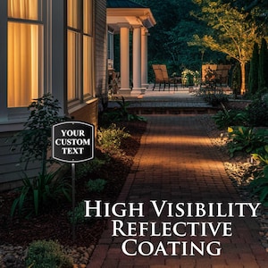 May include: A black and white sign with the text "YOUR CUSTOM TEXT" is displayed on a metal stake. The sign is in front of a house with a brick pathway. The sign also has the text "HIGH VISIBILITY REFLECTIVE COATING".