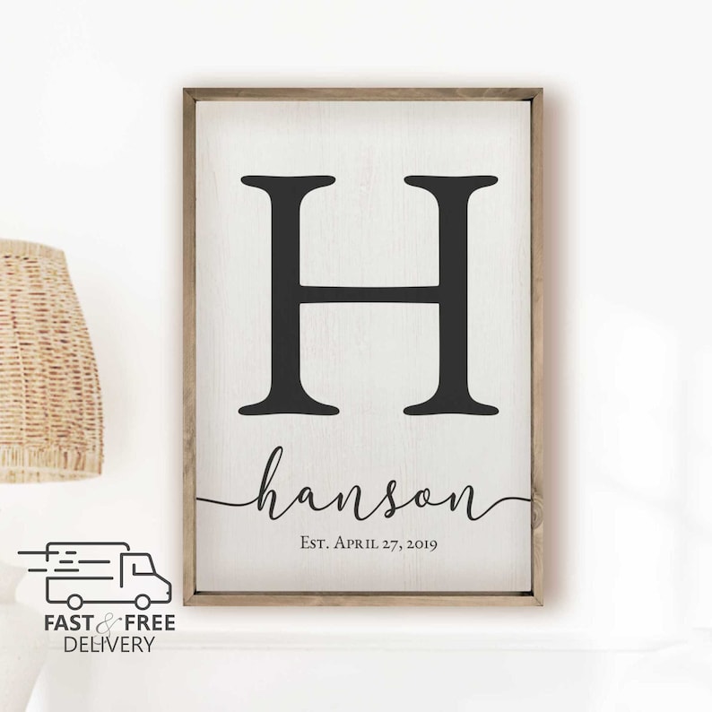 Custom printed personalized family name sign with monogram and established date.  It has a white wood background and natural wood frame handmade in Brownsburg, Indiana. An icon displays the message Fast and Free Delivery.