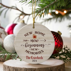 May include: A round, white, wooden ornament with the text "NEW HOME new beginning NEW MEMORIES The Crawfords 2024". The ornament has a red heart and a small house illustration.