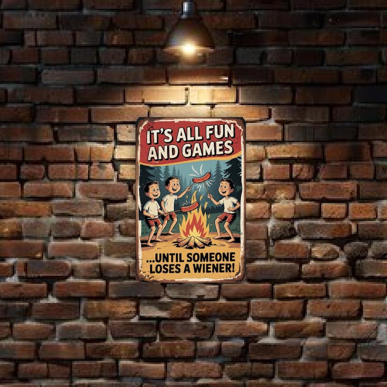 May include: A rectangular metal sign with a retro illustration of three children roasting hot dogs over a campfire. The sign reads "IT'S ALL FUN AND GAMES...UNTIL SOMEONE LOSES A WIENER!" The sign is mounted on a brick wall.