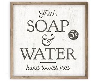 May include: A white wooden sign with a brown frame, featuring the text "Fresh SOAP & WATER hand towels free" in a vintage style font. The sign also includes a small circle with the text "5¢" inside.