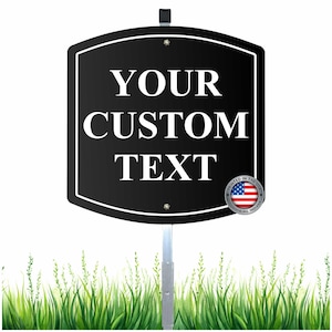 May include: A black sign with white text that reads "YOUR CUSTOM TEXT". The sign is mounted on a metal pole and has a white border. A small emblem with the American flag is in the lower right corner.