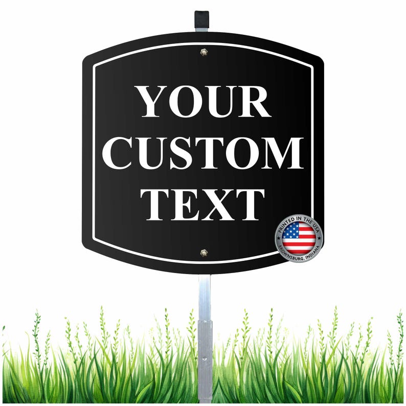 May include: A black sign with white text that reads "YOUR CUSTOM TEXT". The sign is mounted on a metal pole and has a white border. A small emblem with the American flag is in the lower right corner.