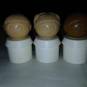 May include: Three vintage Little People figures. Each figure has a round head with a smiling face and a white base. The heads are tan and brown, with different hairstyles. A classic toy for children.