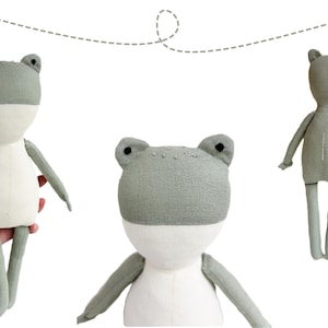 May include: A handmade plush frog toy with a gray and white color scheme. The frog has a simple design with a rounded body and long legs. The toy is made from soft fabric and is suitable for children.