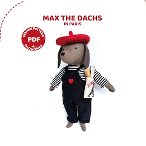 Puede incluir: Un perro salchicha de peluche con boina roja, camisa a rayas y peto negro con un corazón rojo. El perro lleva un bolso tote con una baguette y la Torre Eiffel. El texto dice "Max the Dachs in Paris."