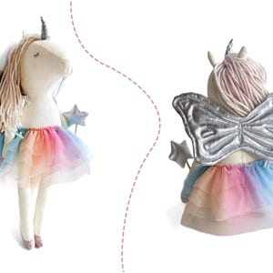 K&ouml;nnte beinhalten: Eine Pl&uuml;sch-Einhorn-Puppe mit silbernem Horn und Fl&uuml;geln sowie einem Regenbogen-Tutu. Die Puppe hat lange, hellfarbene Haare und h&auml;lt einen sternf&ouml;rmigen Zauberstab. Die Fl&uuml;gel sind silberfarben und das Tutu hat einen Farbverlauf.