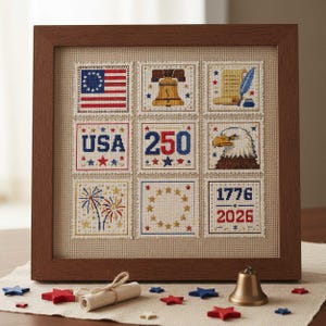 May include: A framed cross-stitch sampler with nine squares, each depicting patriotic symbols. The squares include the American flag, Liberty Bell, and an eagle. The text "USA", "250", and "1776-2026" are also featured. The frame is brown.