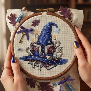 May include: Cross-stitch embroidery in a wooden hoop depicting a blue witch's hat, books, candles, and an owl. The design includes a key, purple ribbon, and decorative elements. The embroidery is held by hands with blue and gold nail polish.