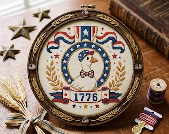 May include: A round, framed cross-stitch featuring a patriotic goose wearing a bow tie and hat, surrounded by stars and ribbons in red, white, and blue. The year "1776" is displayed on a banner. The frame is wood-toned.
