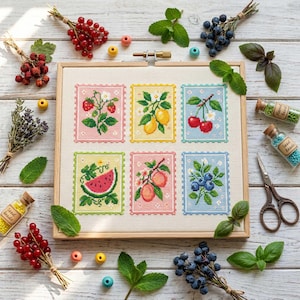 Peut inclure: Une broderie au point de croix avec six motifs de fruits colorés : fraises, citrons, cerises, pastèque, pêches et myrtilles. L'ouvrage est dans un cadre en bois, entouré d'herbes fraîches, de baies et de fournitures de bricolage.