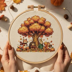 Könnte beinhalten: Ein Kreuzstich-Stickrahmen mit einer Herbstszene. Das Design zeigt einen großen Baum mit orangefarbenen und gelben Blättern sowie verschiedene Waldtiere, darunter ein Fuchs, ein Igel, ein Kaninchen und ein Eichhörnchen. Die Tiere sind von Kürbissen und Herbstlaub umgeben.