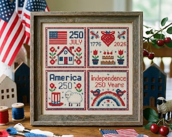 May include: A framed cross-stitch sampler with patriotic themes. The sampler features four squares with images of the American flag, a house, a heart, a cake, a sheep, a rainbow, and the text "250 July", "1776", "2026", "America 250", and "independence 250 Years".