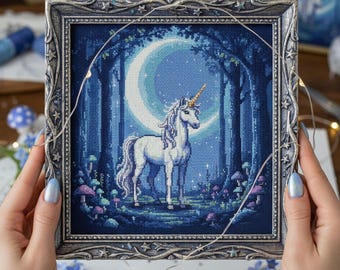 May include: A framed cross-stitch artwork depicts a white unicorn with a golden horn standing in a moonlit forest. The artwork features a crescent moon, tall trees, and colorful mushrooms. The frame is silver with ornate detailing.