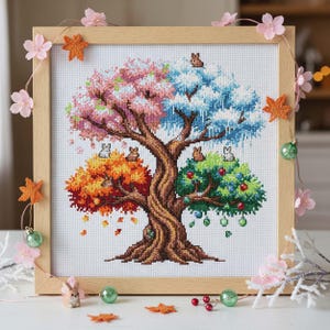 Peut inclure: Broderie au point de croix d'un arbre représentant les quatre saisons. L'arbre présente des fleurs roses, de la neige bleue, des feuilles orange et des fruits verts. De petits lapins sont dispersés dans l'arbre. L'œuvre est encadrée dans un cadre en bois clair et décorée de fleurs roses et d'étoiles orange.