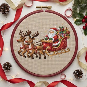 May include: A cross-stitch embroidery of Santa Claus in a red sleigh pulled by two reindeer. The design is set in a round wooden hoop. Red and gold ribbons, pine cones, and greenery surround the embroidery, creating a festive holiday theme.