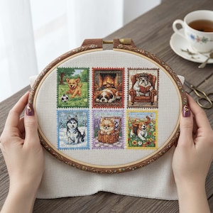 Puede incluir: Un bastidor de bordado de punto de cruz con seis imágenes de perros estilo sello postal. Los perros se representan en varios entornos, incluyendo un paisaje nevado, un sillón acogedor y un campo de flores. El bastidor de madera es redondo y tiene detalles decorativos.
