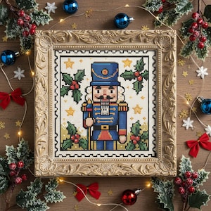 Könnte beinhalten: Kreuzstich-Kunstwerk eines Nussknacker-Soldaten in einem goldenen, verzierten Rahmen. Der Soldat trägt eine blaue Uniform mit goldenen Akzenten und hält einen Stab. Stechpalmen- und Sternakzente umgeben den Soldaten. Weihnachtsdekor mit roten Schleifen, Kugeln und Lichtern.