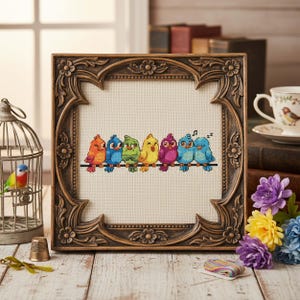 Finished Rainbow Birds Cross Stitch Pattern displayed in a hoop shows seven bright birds perched on a wire, each stitched in a different rainbow shade. Their playful personalities include singing, winking, and dozing off, making the design full of charm. The vibrant palette features oranges, yellows, blues, greens, and purples, balanced with backstitch outlines for clarity. This counted embroidery PDF pattern is perfect for stitchers who love cheerful and whimsical art, creating a handmade
