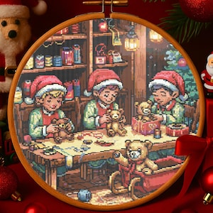 Könnte beinhalten: Kreuzstich-Stickerei in einem Holzrahmen, die drei Figuren mit Weihnachtsmützen zeigt, die Teddybären an einem Werkstatttisch zusammenbauen. Die Szene spielt in einem gemütlichen Raum mit Geschenkregalen und einem Weihnachtsbaum, mit einem Teddybär in einem Schlitten.