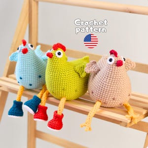 Könnte beinhalten: Drei handgefertigte Häkel-Hühner in Hellblau, Limettengrün und Beige. Jedes Huhn hat einen roten Kamm, weiß-schwarze Augen und baumelnde Beine mit Stiefeln. Der Text Crochet pattern und eine kleine Flagge der Vereinigten Staaten sind zu sehen.