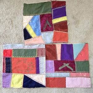 May include: Two rectangular fabric panels featuring a patchwork of multicolored satin and silk-like fabric scraps joined by visible decorative stitching. The panels display embroidered details including a hand outline and pine needle sprigs.