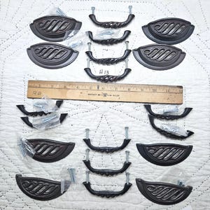 May include: A collection of antique-style cabinet hardware, including decorative pulls and handles. The handles have a twisted rope design, and the pulls feature a leaf-like pattern. The hardware is dark brown and comes with mounting screws.