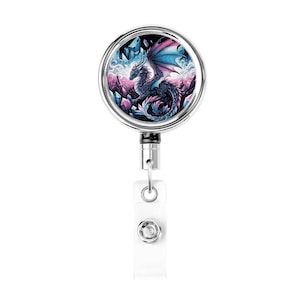 May include: A silver retractable badge reel with a fantasy dragon design. The dragon is depicted with blue and pink wings, perched on a bed of crystals. The background features a misty, ethereal landscape.