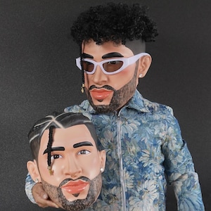 Op de afbeelding: Twee 3D-geprinte hoofden van een man met een baard en krullend haar. Het hoofd links houdt het hoofd rechts vast. Beide hoofden dragen een witte zonnebril.