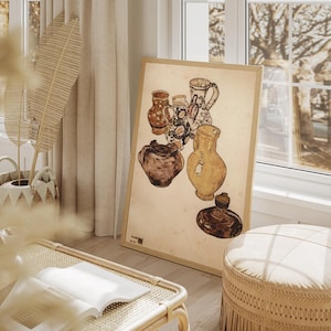 May include: A framed artwork featuring a still life of various antique pottery vessels in shades of brown, yellow, and blue. The artwork is leaning against a wall in a bright, airy room with natural light.