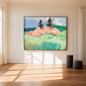 Pode incluir: Grande pintura de paisagem emoldurada retratando duas árvores verde-escuras no topo de uma colina rosa e verde sob um céu azul. A pintura está pendurada em uma parede branca acima de um piso de madeira. Duas pequenas banquetas cilíndricas cinza-escuras com tampas de madeira estão na frente.