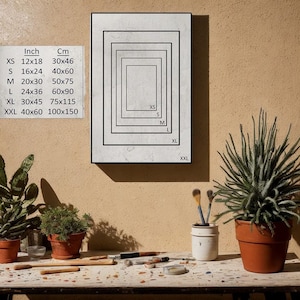 May include: A framed artwork with a series of nested rectangular borders, labeled with sizes XS to XXL. A chart displays inch and centimeter measurements for each size. The artwork is displayed on a beige wall.