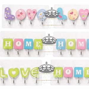 Könnte beinhalten: Dekorative Wandhaken in drei Sets. Das obere Set schreibt "LOVE" mit Buchstabenhaken in Lila, Rosa und Gelb. Das mittlere Set schreibt "HOME" in Grün, Rosa und Blau. Das untere Set schreibt "LOVE HOME" in Grün, Rosa und Blau.
