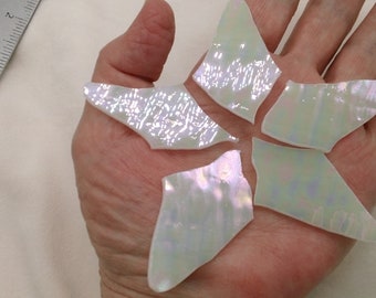 May include: Five iridescent white glass pieces shaped like a star. The pieces are arranged in a star shape on a hand.