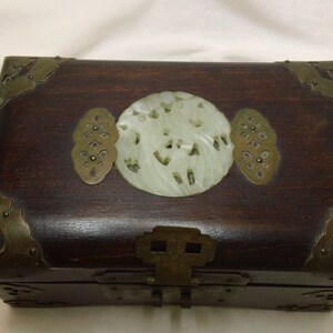 May include: A dark wood box with brass accents and a carved jade inlay. The box has a hinged lid and a brass latch.