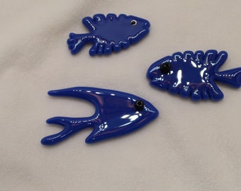 May include: Three blue glass fish ornaments with black eyes. The fish are in different shapes and sizes.