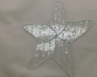 May include: A clear glass starfish ornament with a textured surface. The starfish is made of multiple pieces of glass that have been fused together.