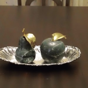 May include: Two green marble fruit sculptures, one pear and one apple, with gold leaf accents, on a silver tray.