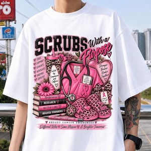 May include: A white t-shirt featuring a graphic design with the text "SCRUBS With a Purpose". The print includes pink medical scrubs, a stethoscope, books, a tumbler, and clogs with leopard print patterns, all accented with pink ribbons.